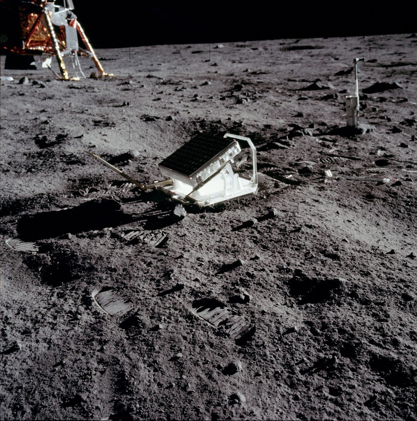 The Apollo 11 laser ranging retroreflector, a suitcase-sized panel of mirrors, sitting on the grey lunar surface with the lunar module and astronaut bootprints behind it.