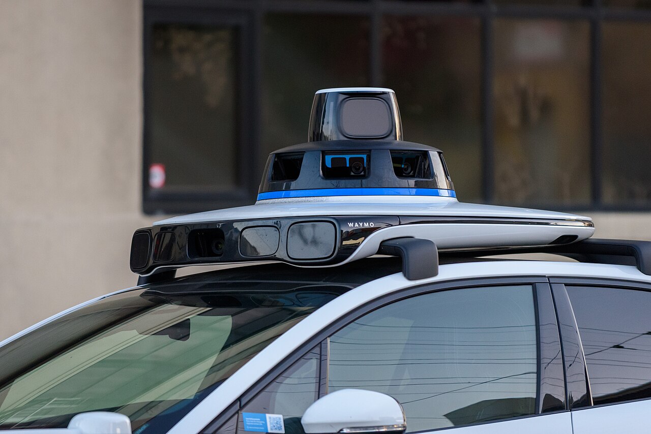 The rooftop sensor module of a Waymo self-driving car: a spinning lidar dome, a ring of cameras, and side sensor pods.