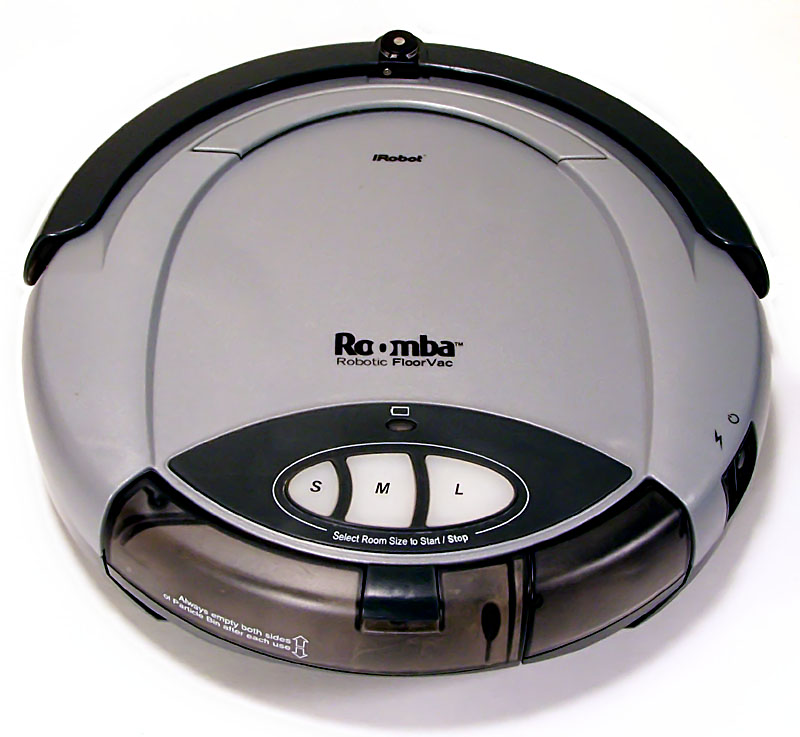 An early circular iRobot Roomba robotic vacuum cleaner sitting on a hardwood floor.