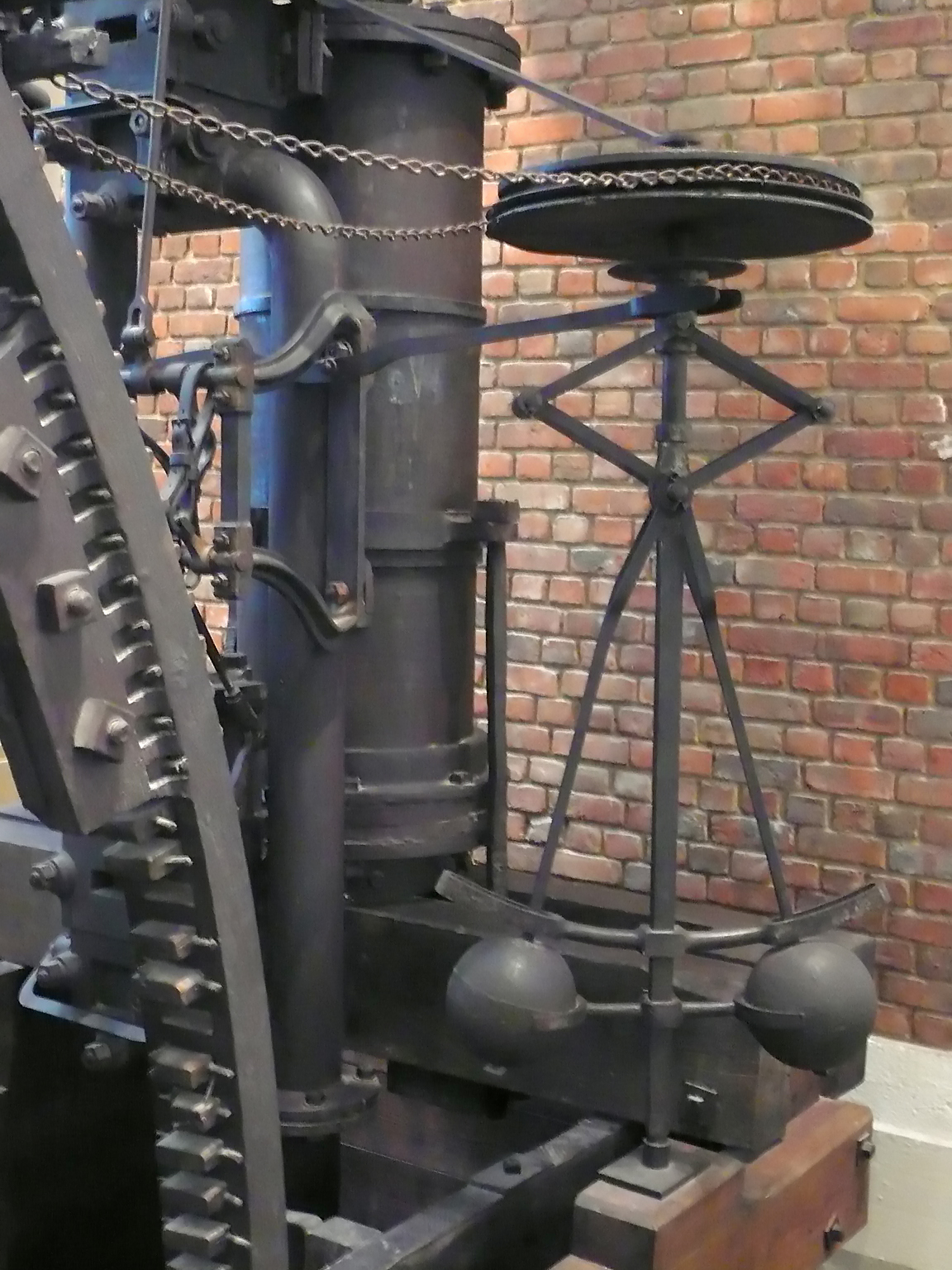 James Watt's centrifugal governor: two brass balls on hinged arms spin around a vertical spindle, rising as speed increases to throttle the steam supply.
